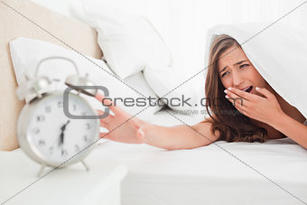 The woman yawns while trying to silence her alarm clock