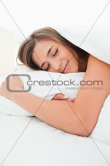 Close up, woman in bed, hand under pillow and smiling