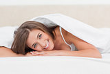 Woman smiling, while lying at the end of the bed, with head on h