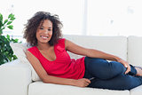 Woman on the couch looking forward and smiling with a phone in h