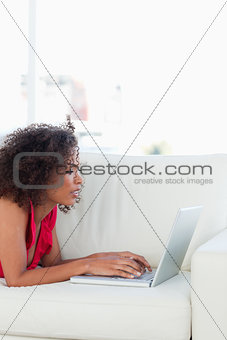 Woman on the couch, looking at and using her laptop