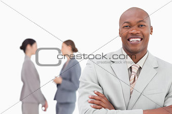 Smiling businessman with folded arms and co-workers behind him