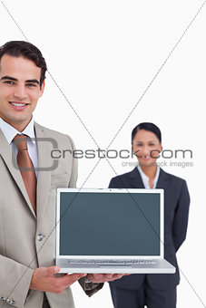 Laptop being presented by smiling salesman with colleague behind