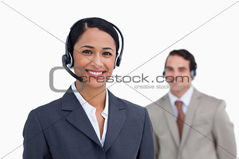 Smiling telephone support employee with colleague behind her