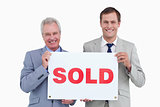 Smiling real estate agents holding sold sign
