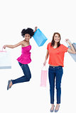 A teenage girl jumping with her shopping bags while her friend i