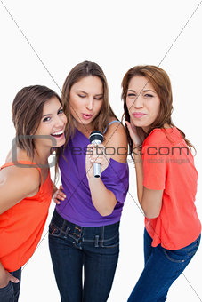 Three attractive young women singing in a microphone