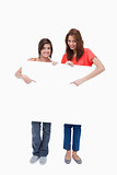 Smiling teenage girls standing upright behind a blank poster whi