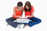 Two cute teenagers sitting cross-legged while looking at a lapto