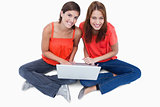 Smiling teenage girls sitting with a laptop on legs while lookin