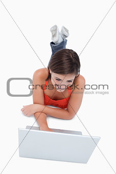 Smart teenage girl lying down in front of a laptop with legs cro
