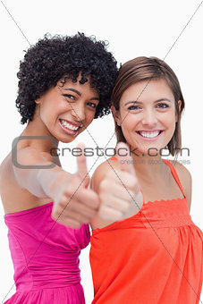 Smiling teenage girls proudly showing their thumbs up against a 