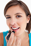 Smiling young woman applying lipstick against a white background