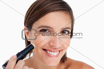 Smiling young woman applying natural foundation on her face