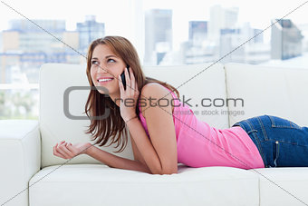 Young smiling woman lying on a sofa while talking on the phone
