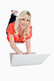 Smiling attractive woman using her laptop while lying on the flo