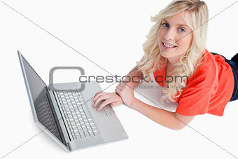 Smiling young woman using her laptop while lying down
