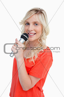 Young blonde woman smiling while singing into a microphone