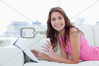 Young woman showing a great smile while reading and drinking cof