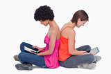 Teenagers sitting cross-legged back to back with a tablet comput