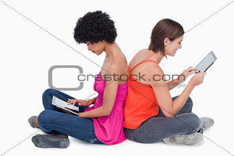 Teenage girl holding her tablet PC in the air while a friend is 