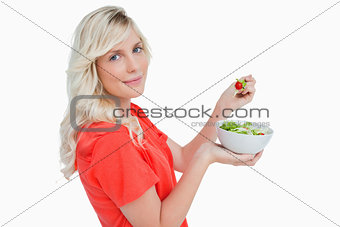 Side view of a young blonde woman eating vegetable salad