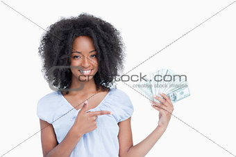 Young smiling woman pointing her finger on a fan of dollar notes