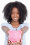 Pink piggy bank held by a young smiling woman with curly hair