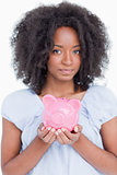 Young woman holding a pink piggy bank close