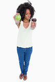 Young woman holding a muffin and a green apple and hesitating