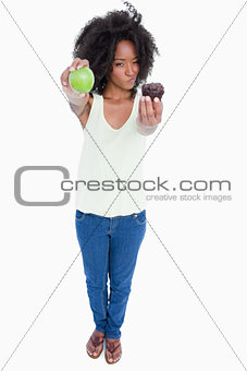 Young woman holding a muffin and a green apple and hesitating