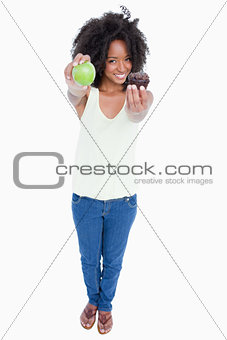 Smiling young woman holding an apple in one hand and a muffin in