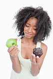 Young woman hardly hesitating between a muffin and an apple