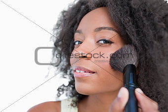 Young woman applying make-up while using a powder brush