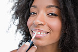 Young smiling woman making-up while using a lip gloss applicator