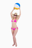 Smiling teenager in a pink swimsuit raising a beach ball above h