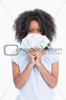 Young curly woman hiding her face behind a fan of dollars