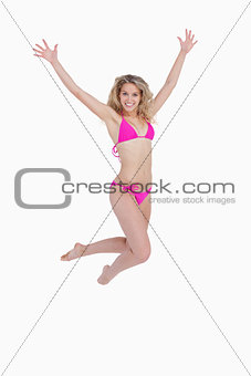 Smiling blonde woman jumping while raising her arms