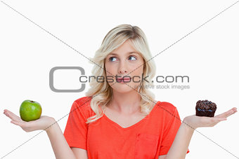 Woman hesitating between a chocolate muffin and a green apple