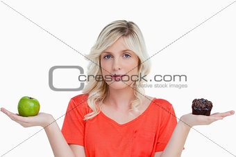 Young woman looking at the camera while holding a muffin and a g