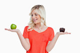 Young woman holding an apple and a muffin while looking at the a