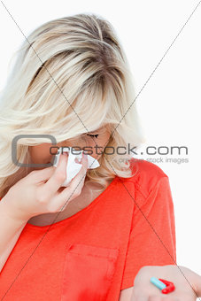 Young woman sneezing while holding some tablets