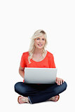 Smiling young woman using her laptop while sitting cross-legged