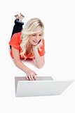 Young blonde woman lying on the floor while using a laptop