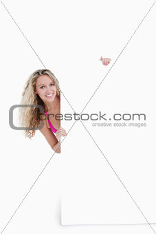 Smiling teenager hiding her body behind a blank poster