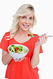 Young smiling woman eating a fresh salad with a fork