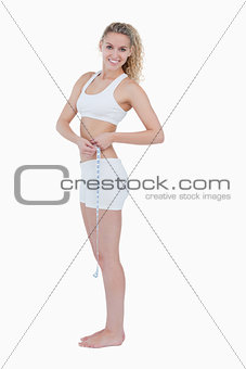 Smiling teenager standing up while measuring her waist