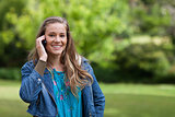 Young smiling girl talking on the phone while standing in a park