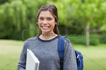 Young happy adult coming back from school while holding a notebo