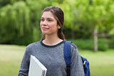 Young smiling woman looking far away while standing in a park wi